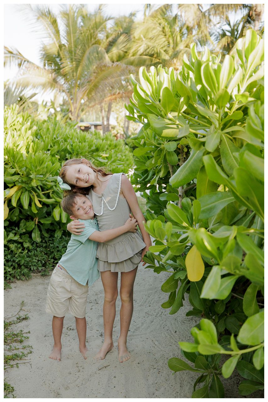 W Punta Mita family photos, two children hugging on a sandy path surrounded by tropical greenery and palm trees.