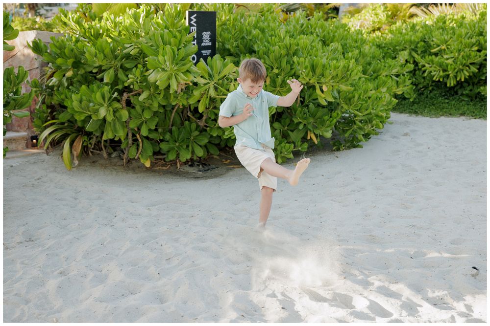 Punta Mita beach family session, child kicking sand on a tropical beach surrounded by coastal greenery.