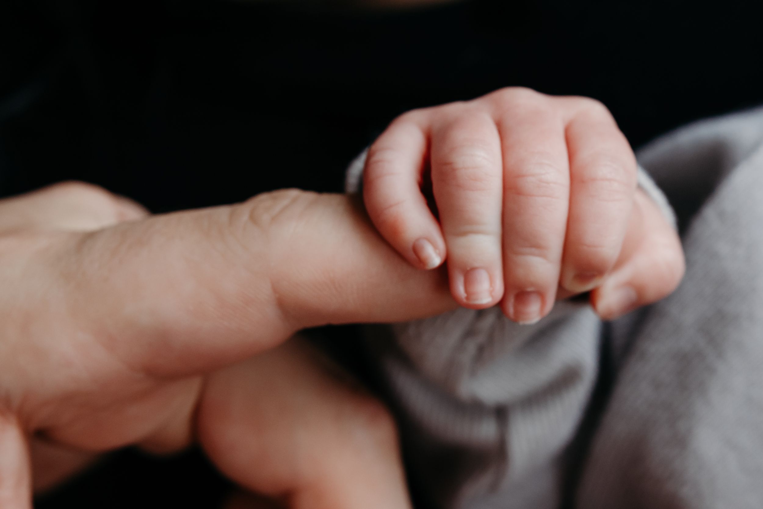 A newborn baby's tiny hand gently gripping an adult's finger, symbolizing new life and parental bond.