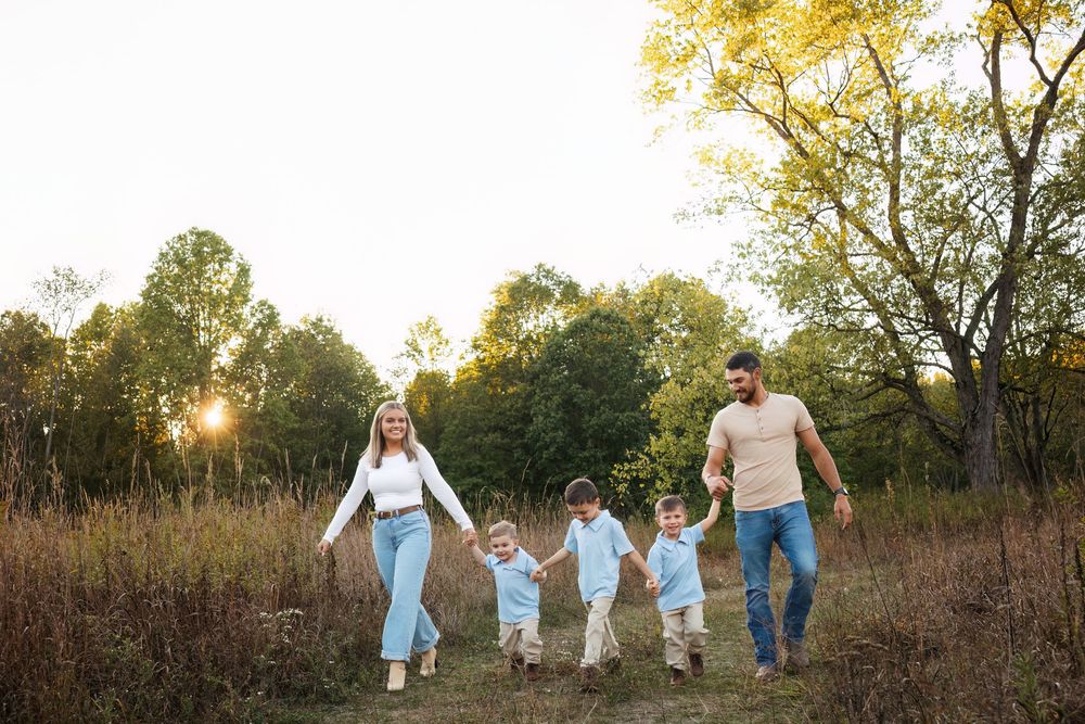 Family of five walking hand-in-hand through a sunlit meadow during golden hour in autumn.