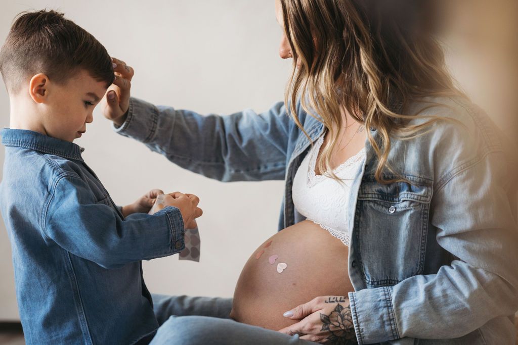 Young boy placing a heart sticker on pregnant mother's baby bump during a maternity photo session.