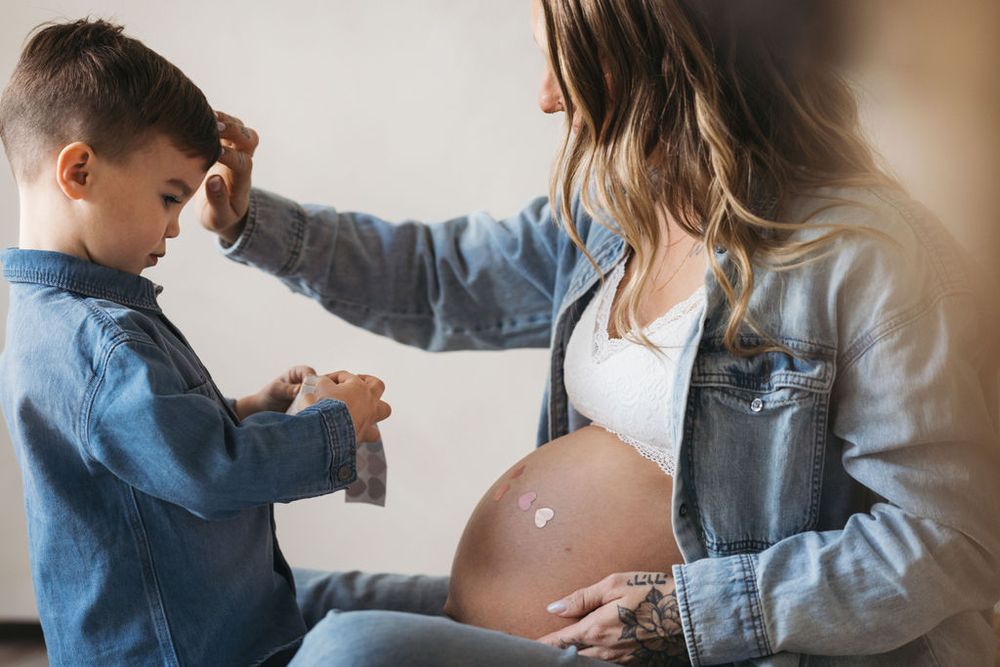 Young boy placing a heart sticker on pregnant mother's baby bump during a maternity photo session.