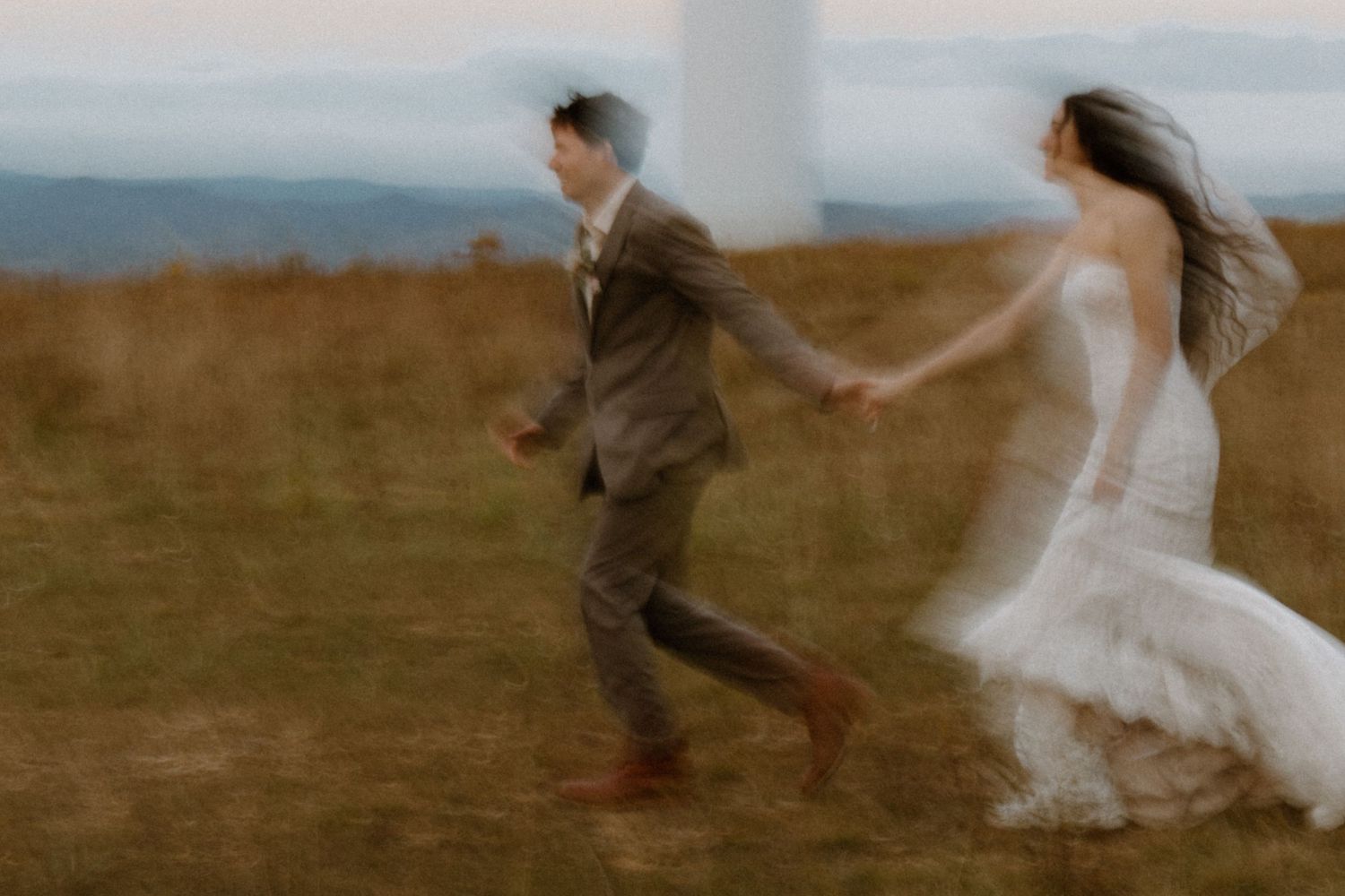Bride and groom running hand in hand through mountain meadow at golden hour.