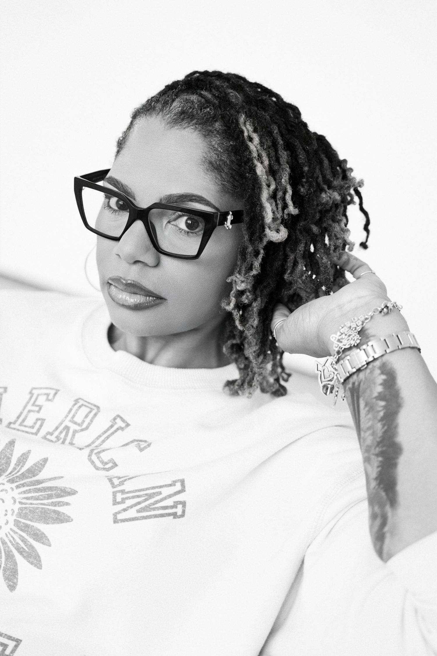 Black and white portrait of a woman with locs and bold glasses in an American graphic tee.