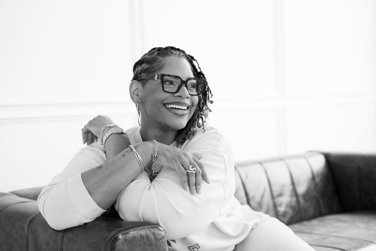 Woman in white outfit smiling while relaxing on a sofa in a black and white photo.