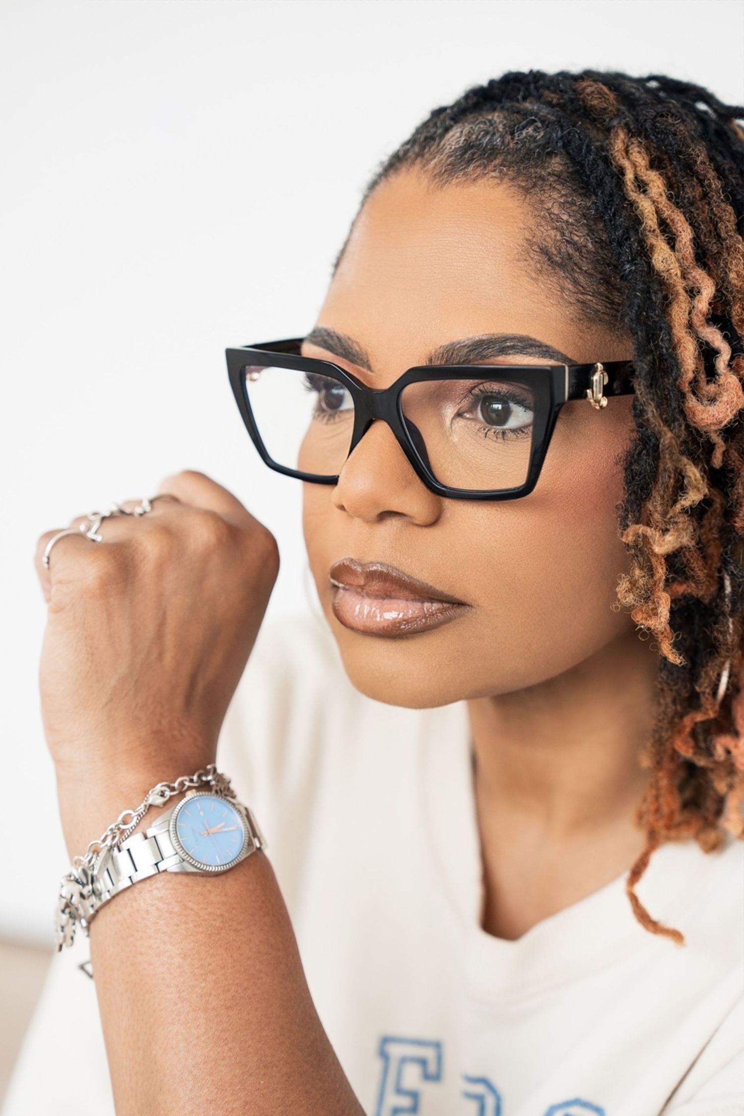 Close-up portrait of woman with locs wearing black glasses and silver watch bracelet.