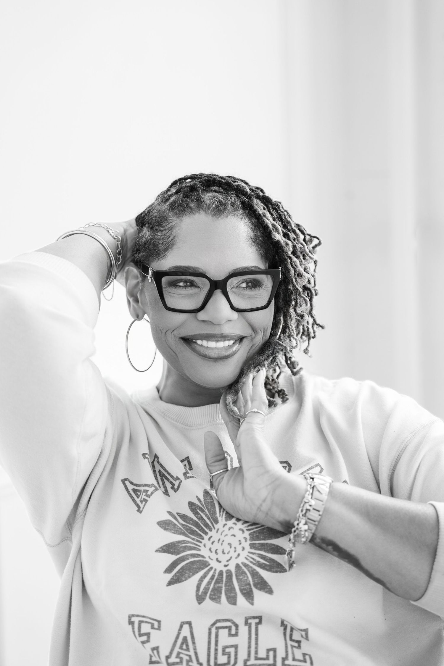Smiling woman in Eagle sweatshirt with braids and glasses posing in black and white portrait.