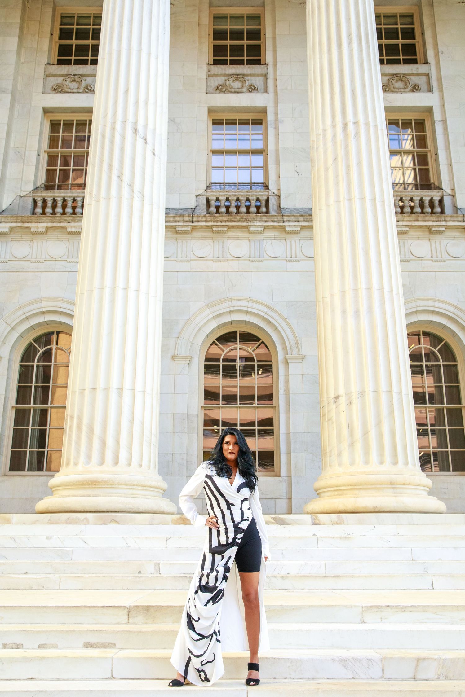 Woman in black and white outfit posing on steps of neoclassical building with large columns.