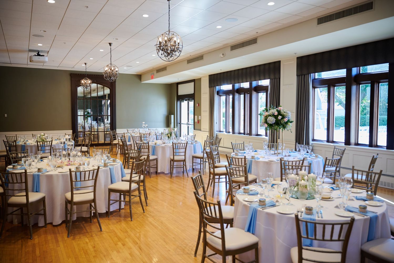 Elegant wedding reception venue with round tables, white linens, chiavari chairs, floral centerpieces, and hardwood floors.