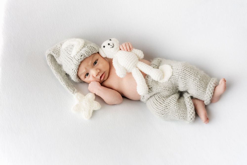 Sleeping newborn baby in gray knit hat and pants cuddling a stuffed bunny toy.