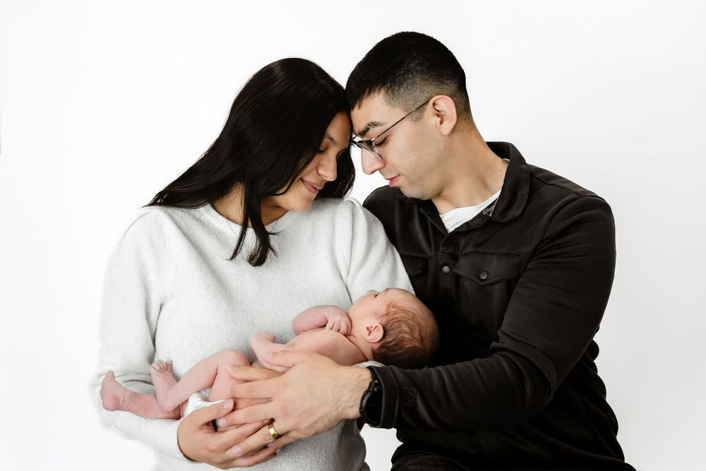 Asian couple tenderly holding newborn baby together against white background.