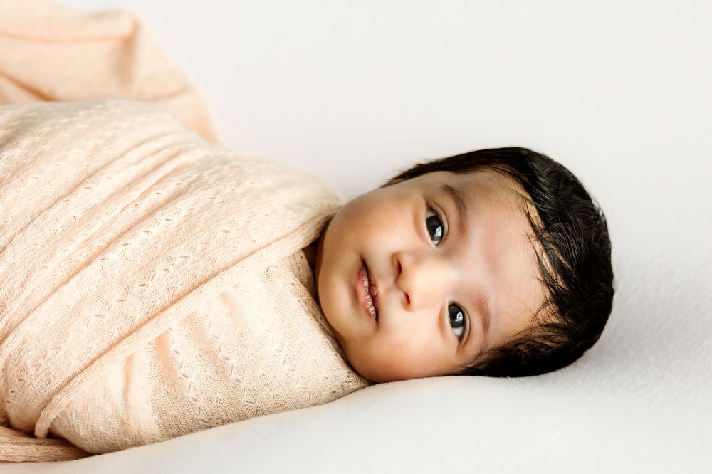 Peaceful newborn baby swaddled in soft peach wrap lying on white background.