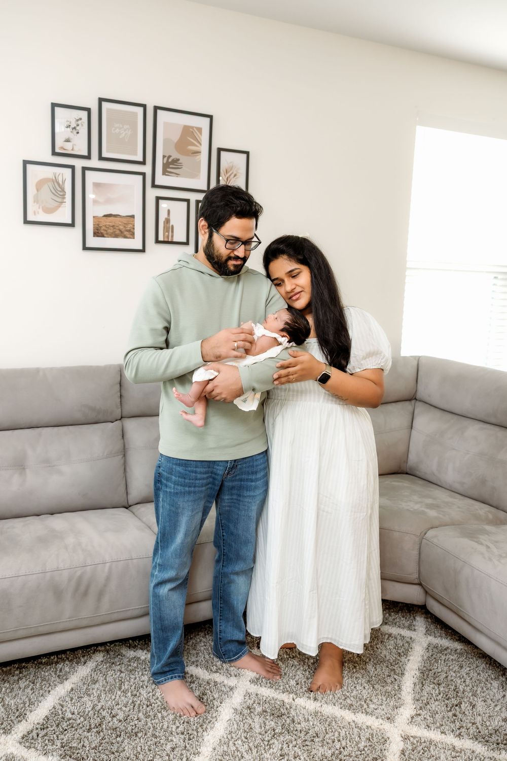 Happy new parents holding their newborn baby in a modern living room with gallery wall.