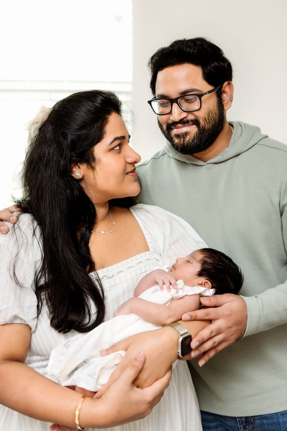 Loving parents smiling at each other while cradling their newborn baby together.