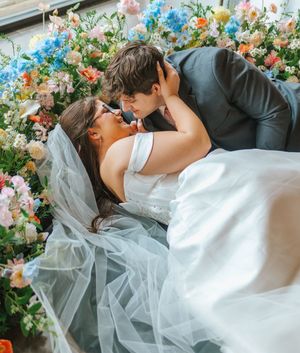 A bride and groom share a romantic kiss lying among colorful flowers at their wedding ceremony.