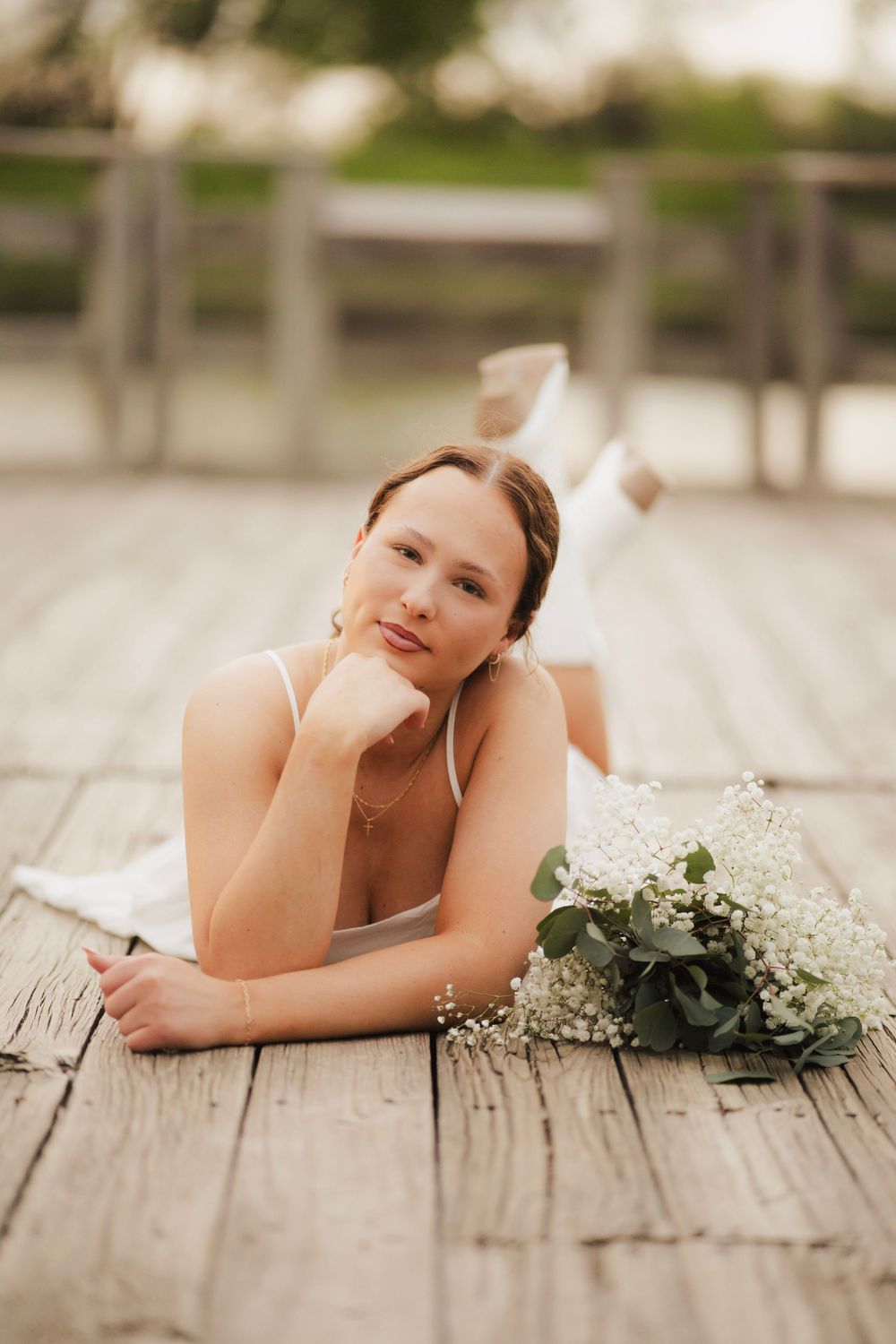 Young woman in white dress lying on wooden dock with baby's breath bouquet nearby.