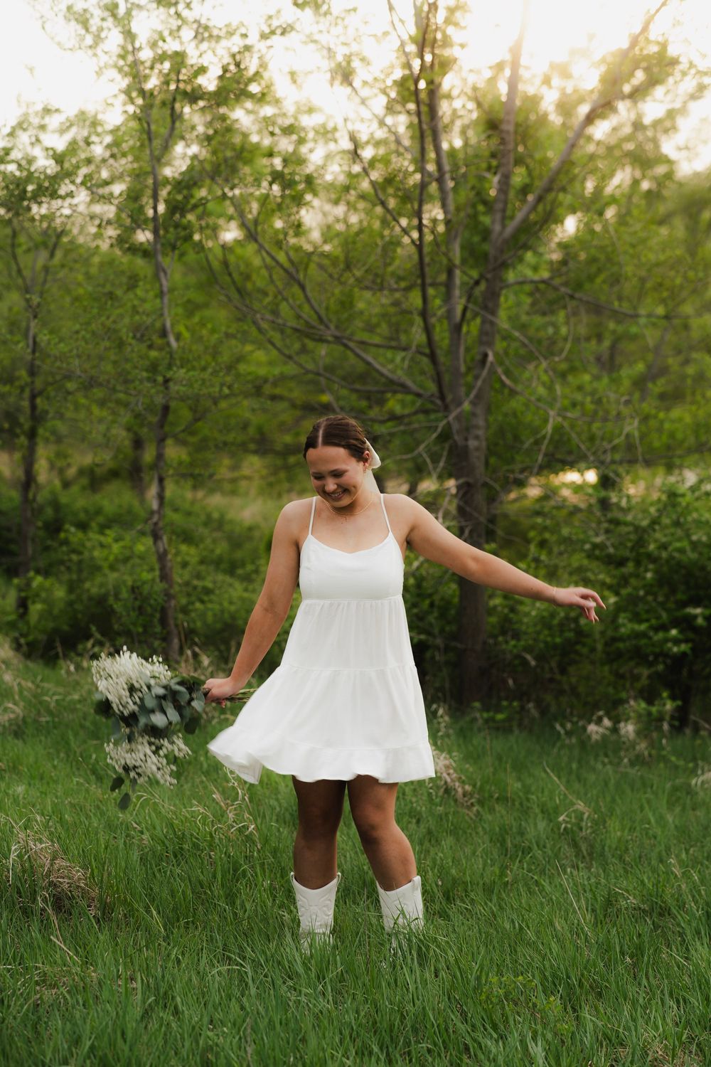 A young woman in a white sundress and boots twirling happily in a lush green meadow at sunset.