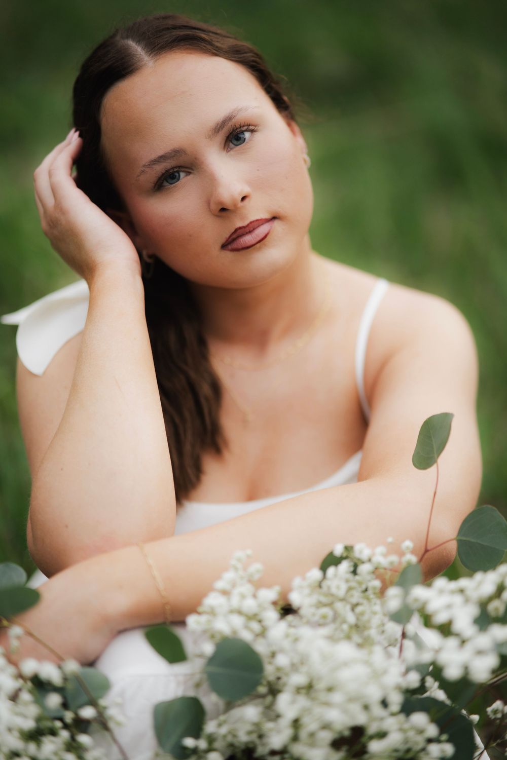 Young woman in white dress gazing at camera while holding bouquet of white gypsophila flowers in green field.