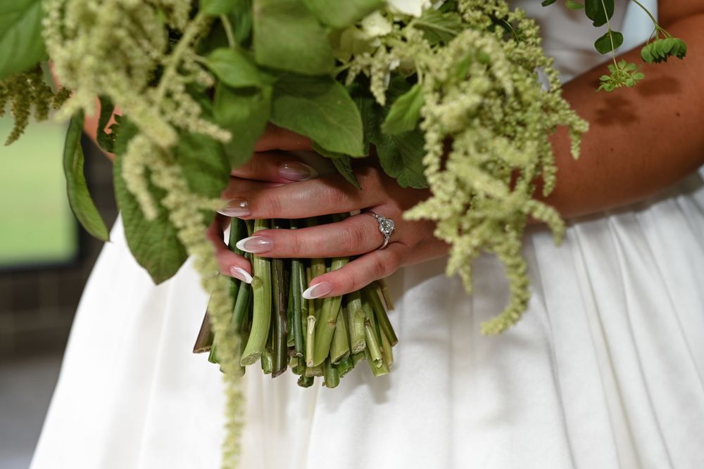 A close-up view of delicate white and green floral wedding bouquets being held against white dresses.