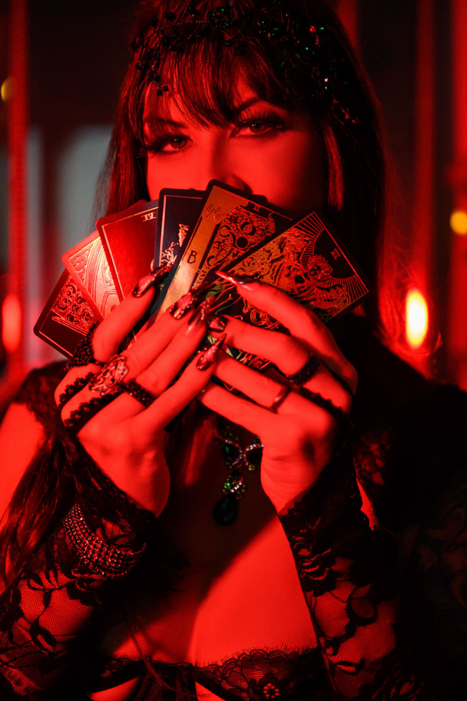 Mysterious figure in red lighting holds up playing cards while wearing black lace. editorial boudoir photography New Orleans.