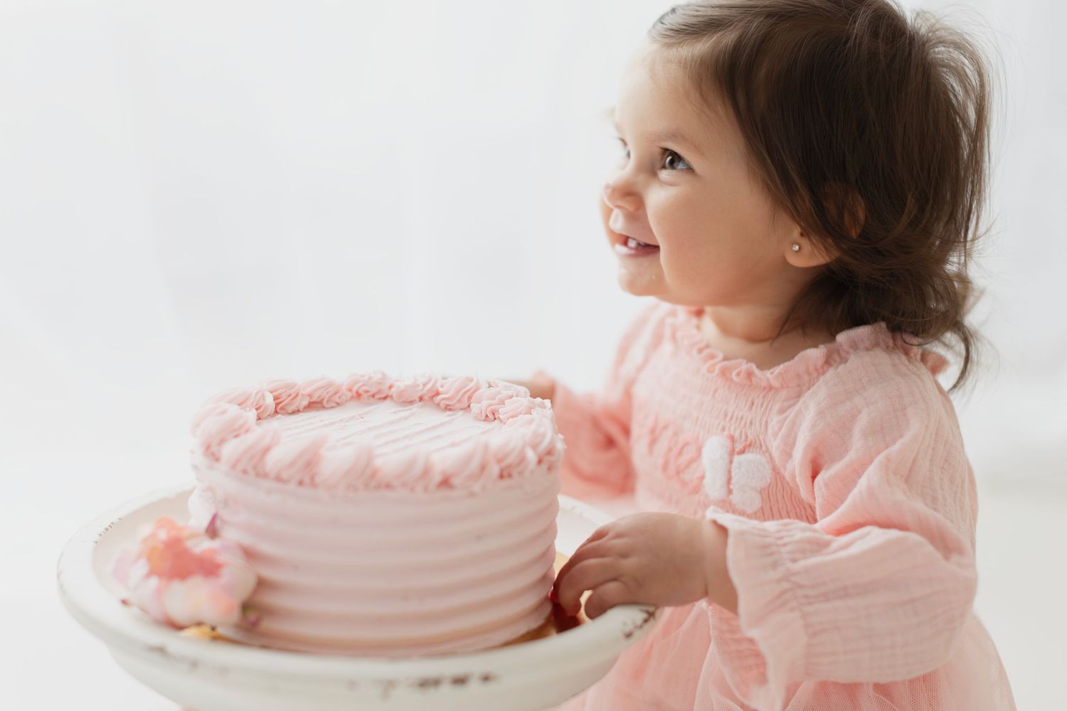 Smiling toddler girl in pink dress holding a pink birthday cake, perfect for first birthday celebration photos. Elizabeth Lang Photography