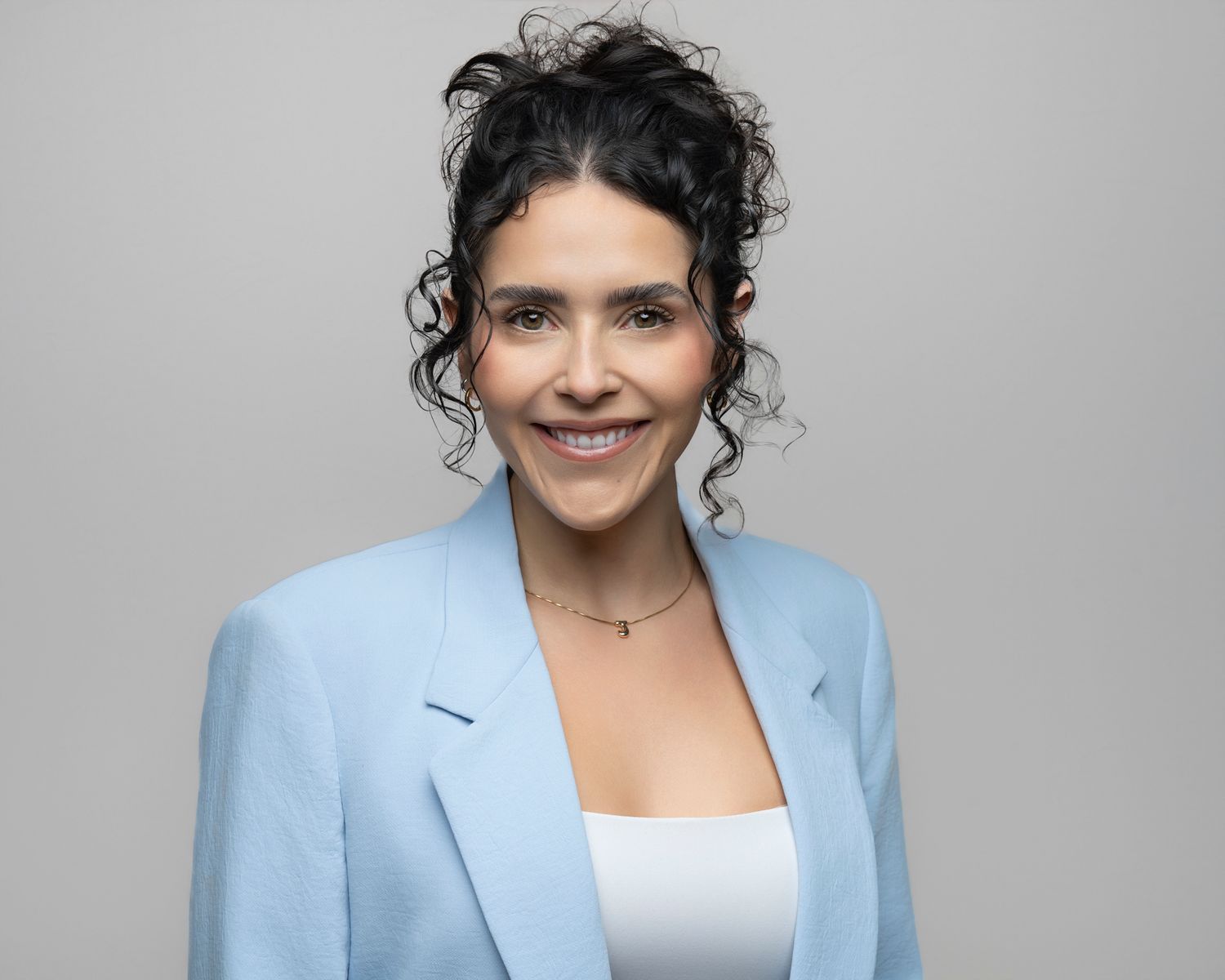 Professional headshot of a smiling woman with short hair wearing a black top against a gray background.