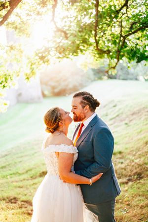 Bride and groom walk hand-in-hand on a forest path, she in a white gown with sunflowers, he in a blue suit.