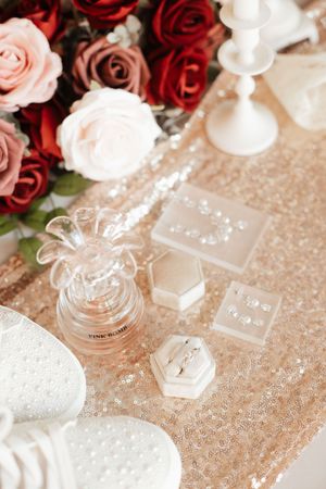 Gold sequin table with wedding rings, perfume, earrings, and red and pink rose bouquet arrangement.