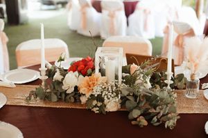 Elegant wedding table centerpiece with red, peach, and white flowers, eucalyptus greenery, candles, and a gold sequin runner.