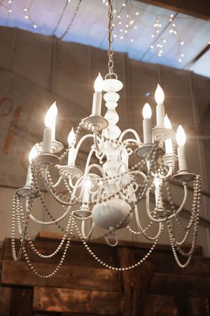 Elegant white chandelier with candle lights and pearl bead garlands hanging in a rustic venue.
