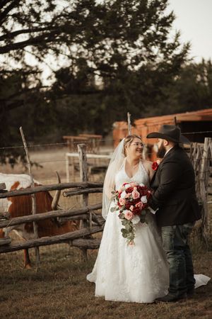 Bride and groom share a romantic moment at a rustic ranch wedding, with cattle and wooden fences in the background.