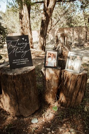 In loving memory wedding display with framed photos on tree stumps and a chalkboard sign honoring deceased loved ones.
