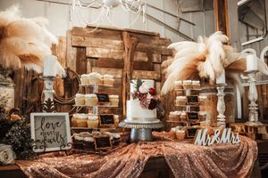 Rustic wedding dessert table with white cake, pampas grass, rose gold sequin tablecloth, and Mr. & Mrs. sign in barn setting.