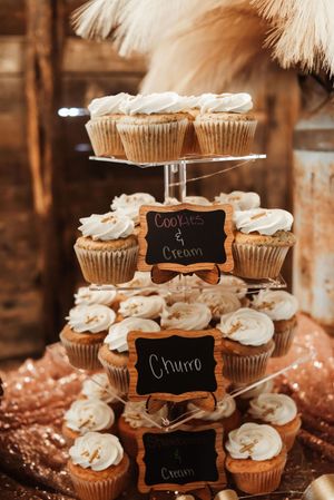 Tiered cupcake stand with cookies and cream and churro flavored cupcakes topped with white frosting at a rustic wedding.
