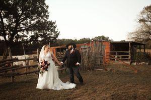 Bride and groom walk hand-in-hand at a rustic farm wedding venue during golden hour.