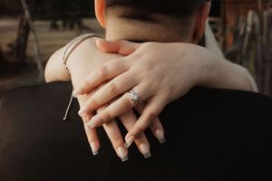 Close-up of a bride's hand with diamond engagement ring resting on groom's shoulder during wedding.