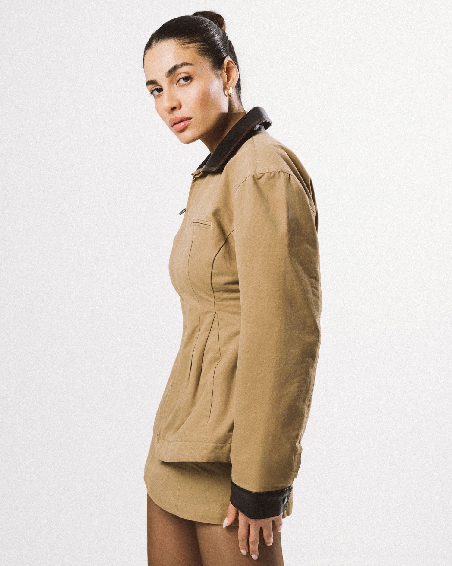 Woman wearing a fitted tan jacket with dark brown collar and cuffs, paired with matching shorts, side profile view.
