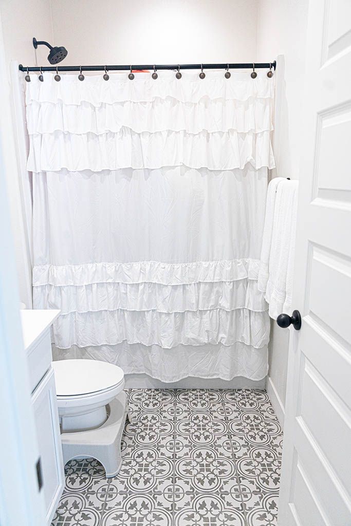 Photography Studio in Murrieta; White bathroom with ruffled shower curtain, black fixtures, and decorative patterned tile floor.