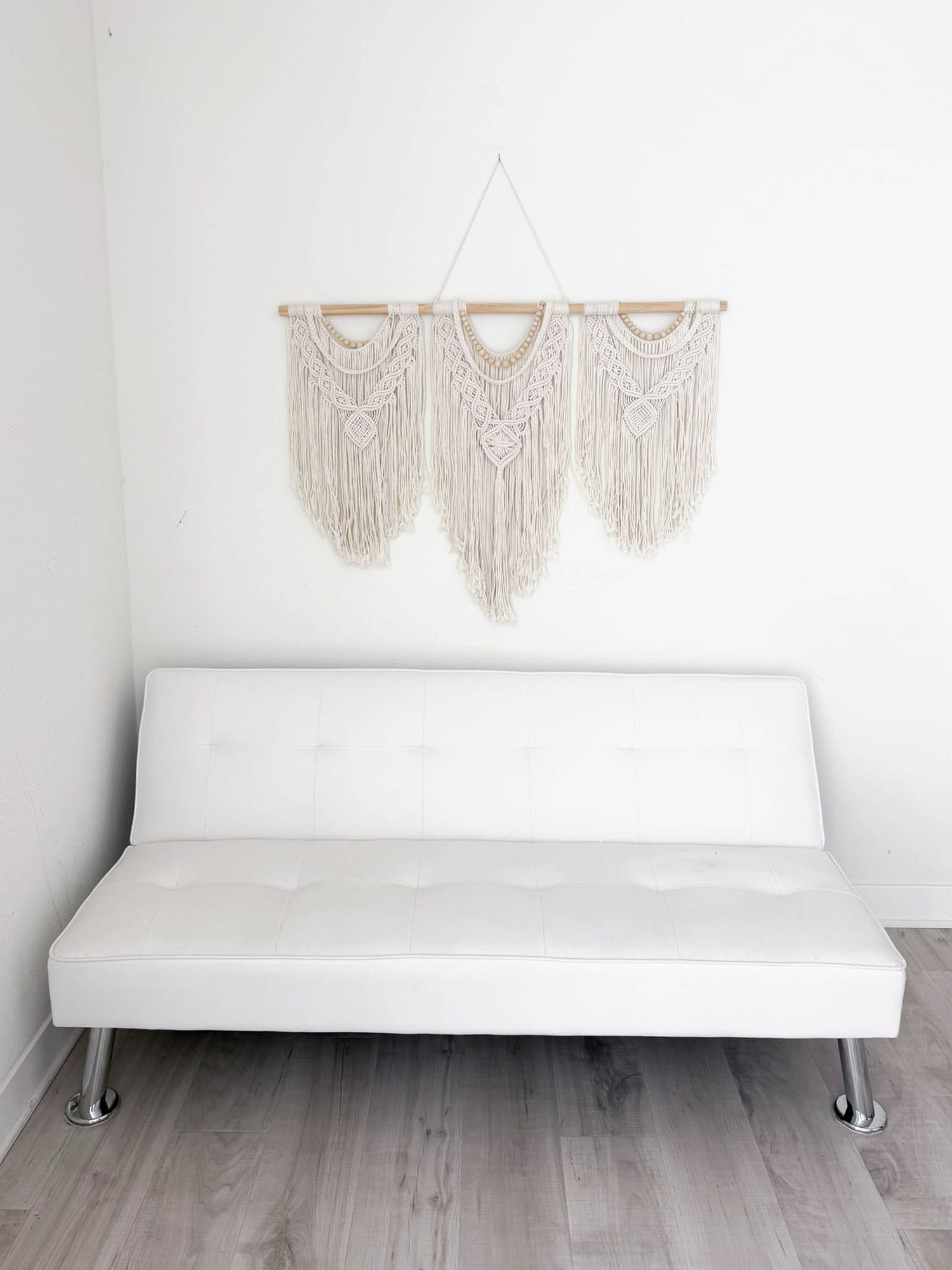 Murrieta Photography Studio; White macrame wall hanging with fringe above a white tufted leather futon on light wood floor.