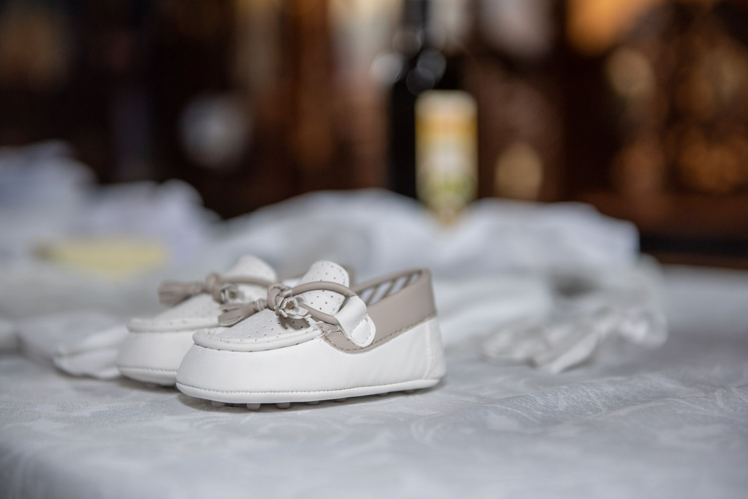 Tiny white baby shoes with bow detail on white linen table for a christening ceremony.