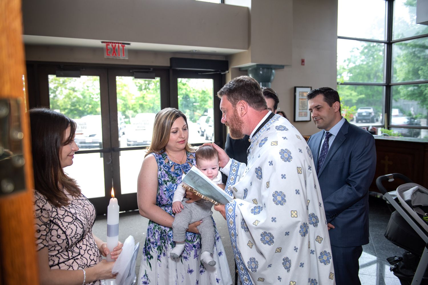 Orthodox priest reading prayers over baby held by mother during baptism ceremony.