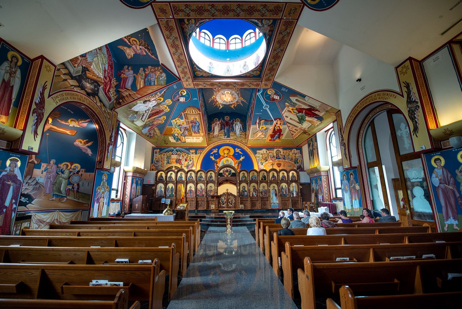 Stunning interior of Orthodox church with elaborate ceiling murals, icons, and wooden pews.