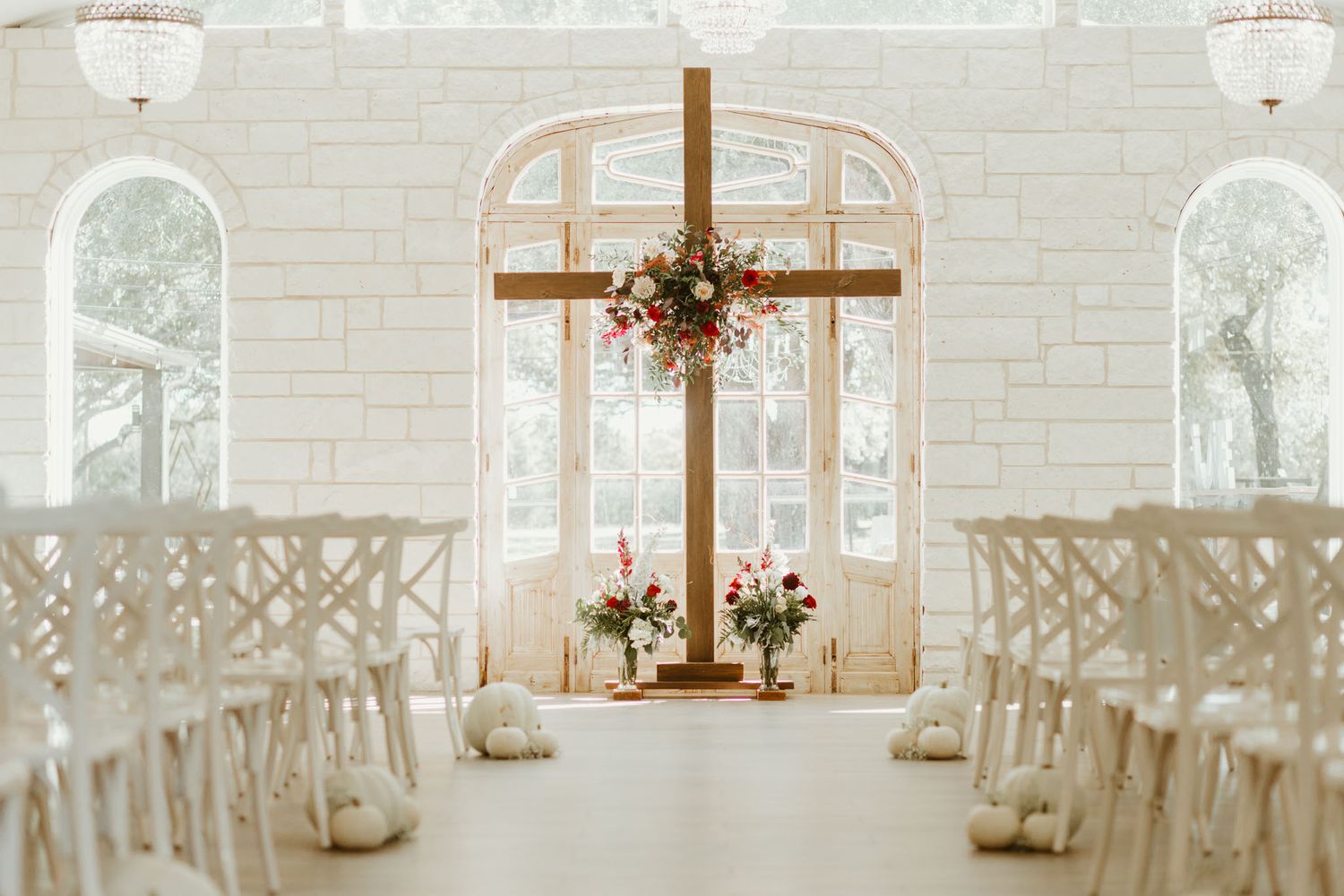 Elegant white chapel wedding ceremony setup with wooden cross and floral decorations.