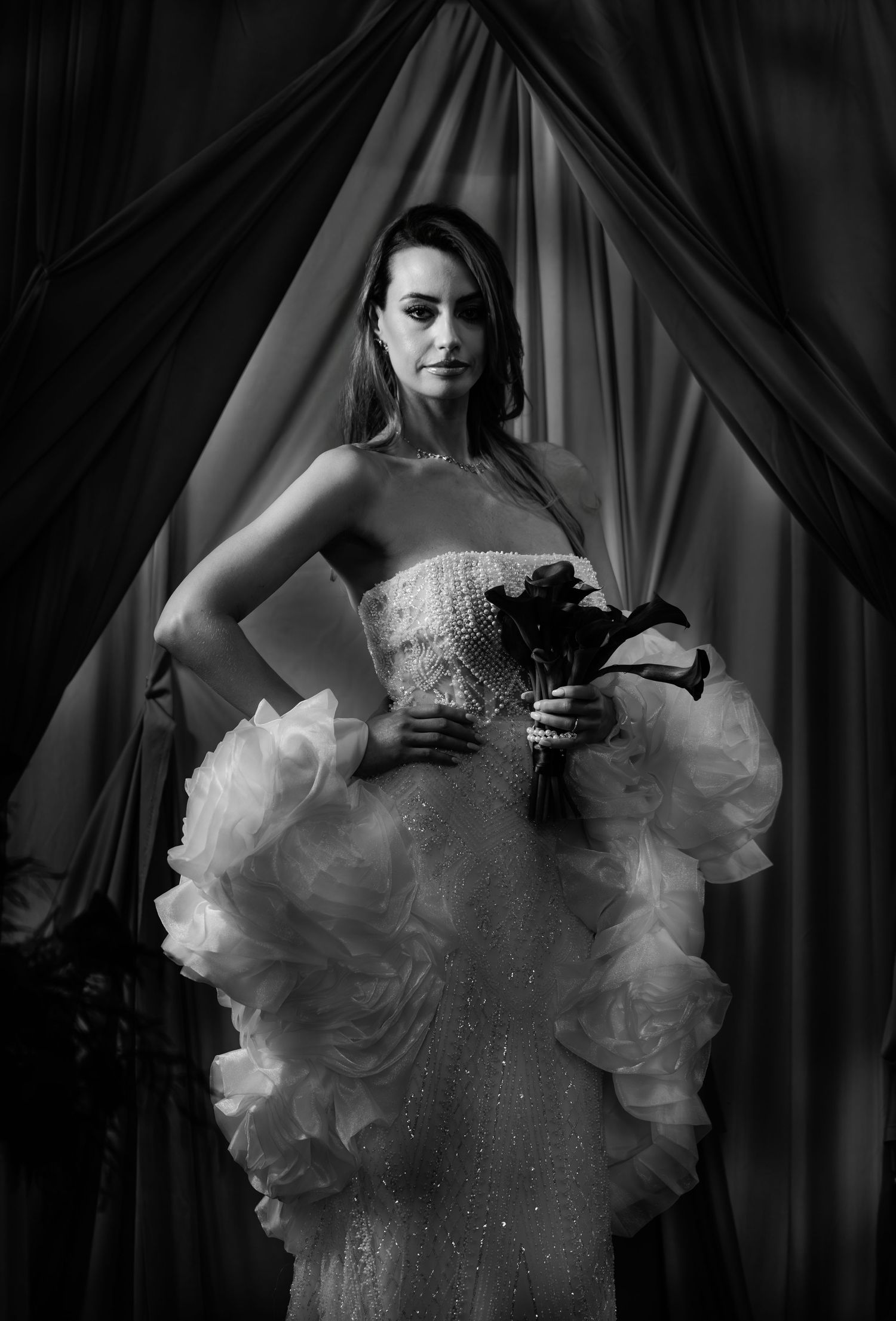 Black and white bridal portrait of a woman in a strapless ruffled gown holding a bouquet.