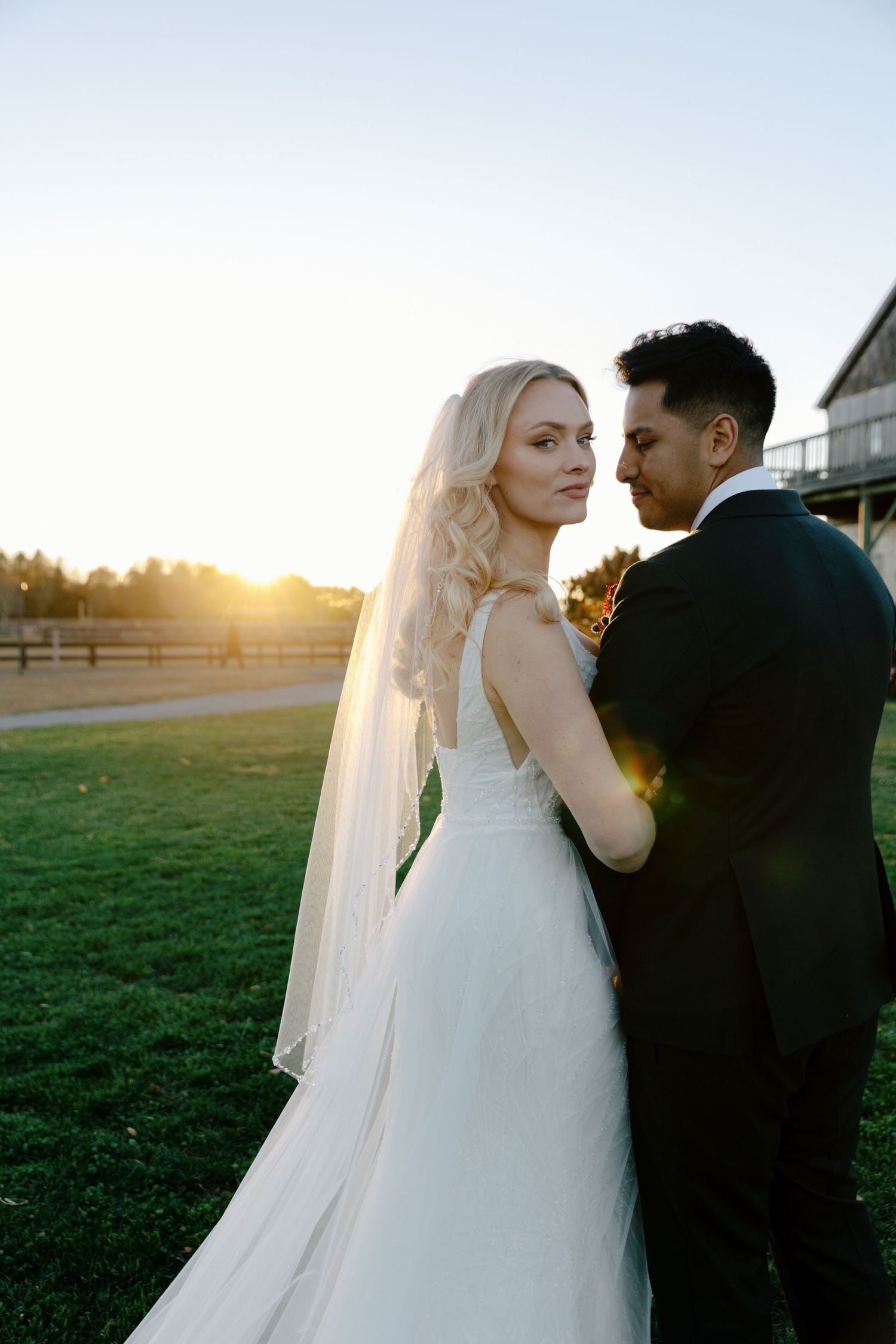 A bride and groom share intimate moments at sunset in a field during their wedding photoshoot.