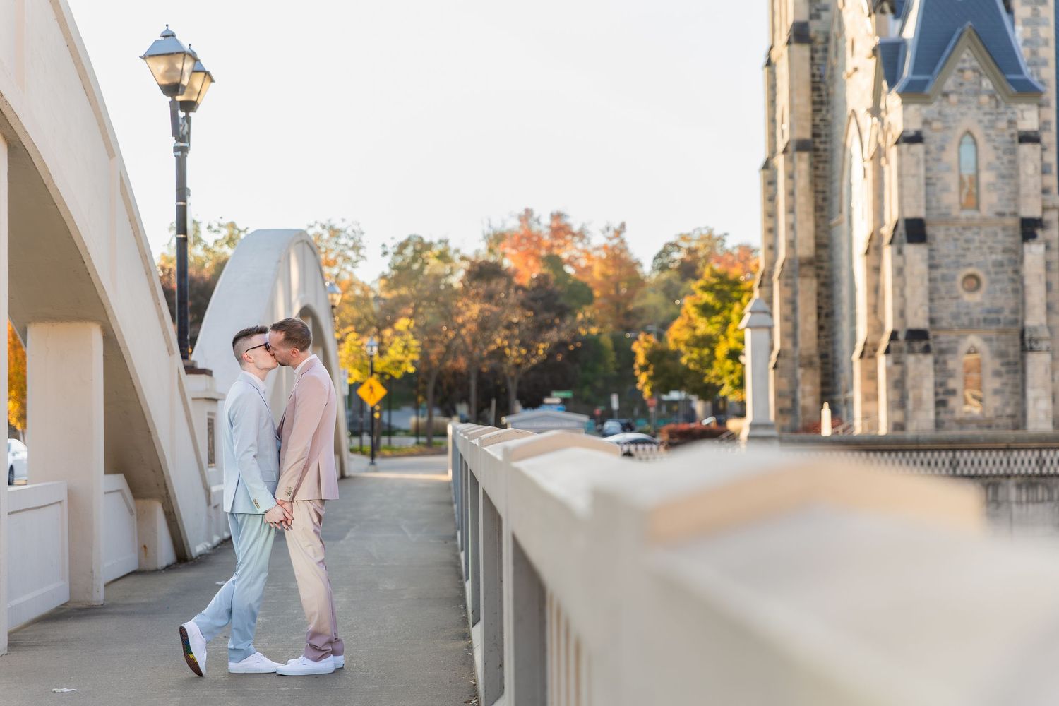 Inclusive wedding photography of two grooms share a kiss on a bridge beside a church in downtown galt in Cambridge, Ontario.