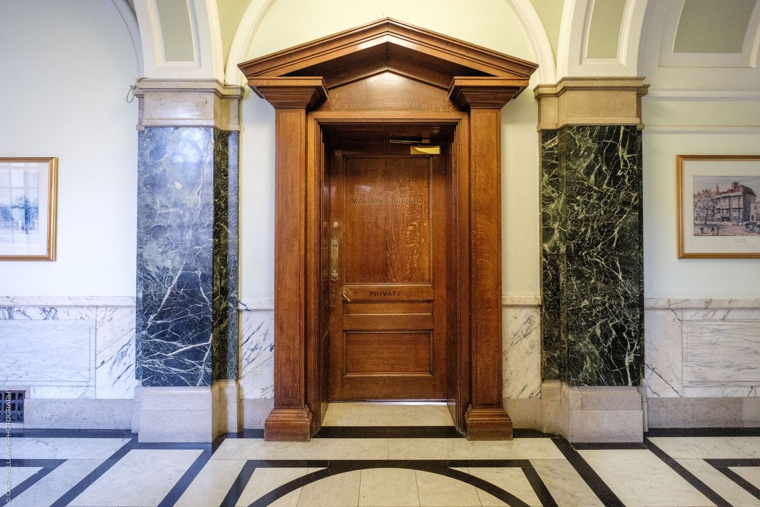 Elegant wooden door flanked by green marble columns in a grand classical building with ornate tile floors.