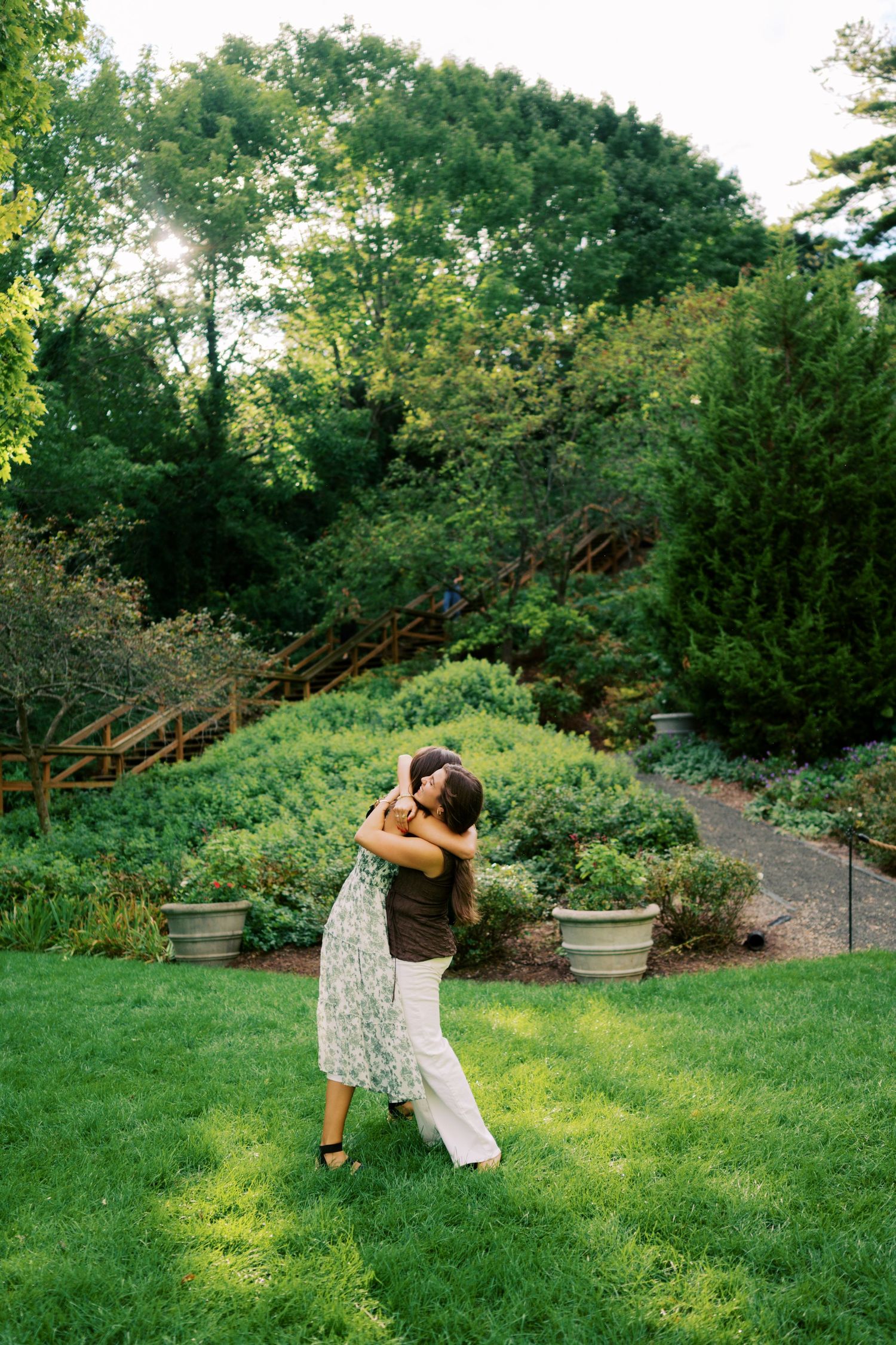 Couple embracing and dancing on lush green lawn in a beautiful garden with trees and shrubs in background.