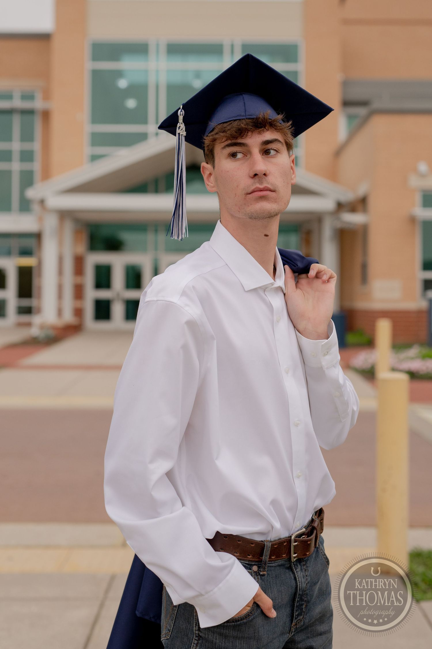 Close-up portrait of graduate in cap and gown outside modern school building.