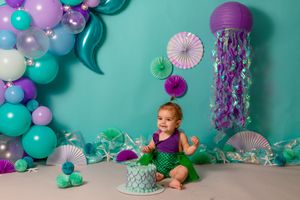 mermaid theme cake smash. toddler girl wearing mermaid outfit eating blue mermaid print cake